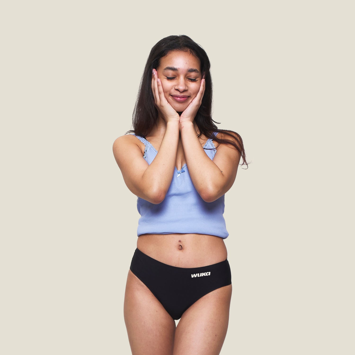 Teen girl smiling with hands on cheeks wearing WUKA Teen Stretch™ Super Heavy Period Pants in black – comfortable and leak-proof period underwear for teenagers.