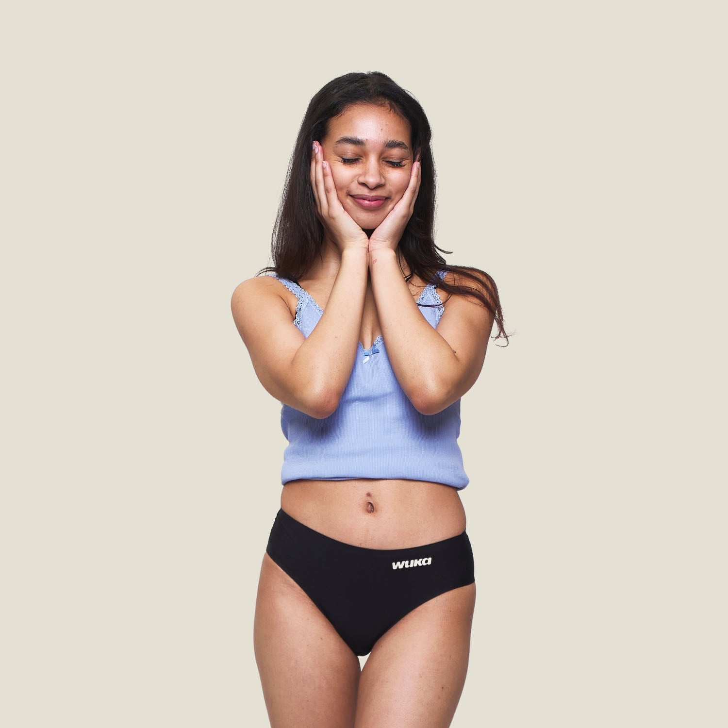 Teen girl smiling with hands on cheeks wearing WUKA Teen Stretch™ Period Pants in black, comfortable and leak-proof period underwear for teenagers.